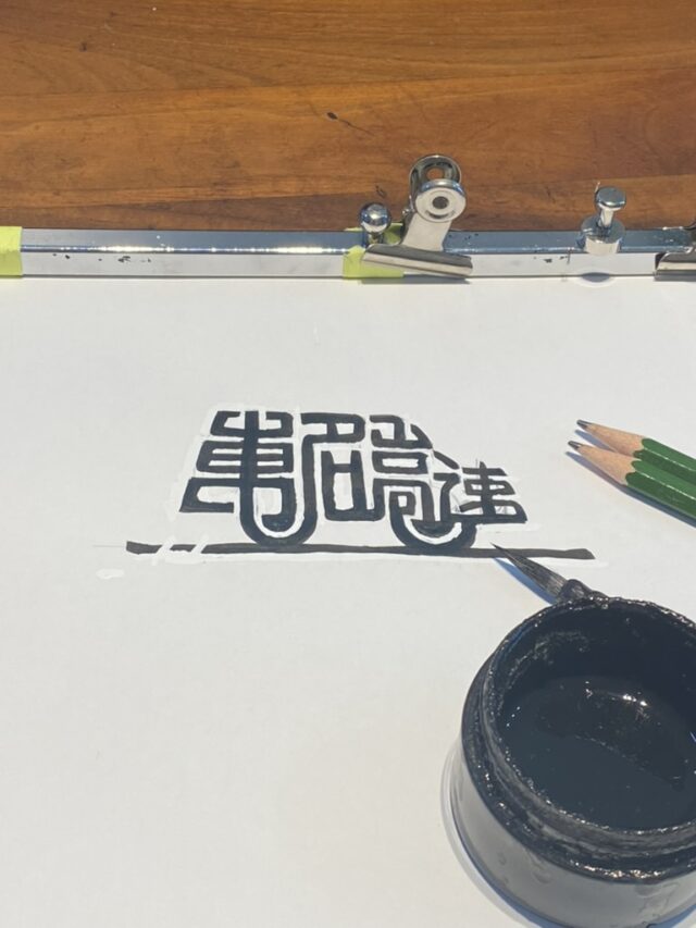 印鑑の文字で車の形をイメージして書いた「東名高速」の手書き作品。下に東・名・高・速の文字が並び、右下に筆先が写っている。